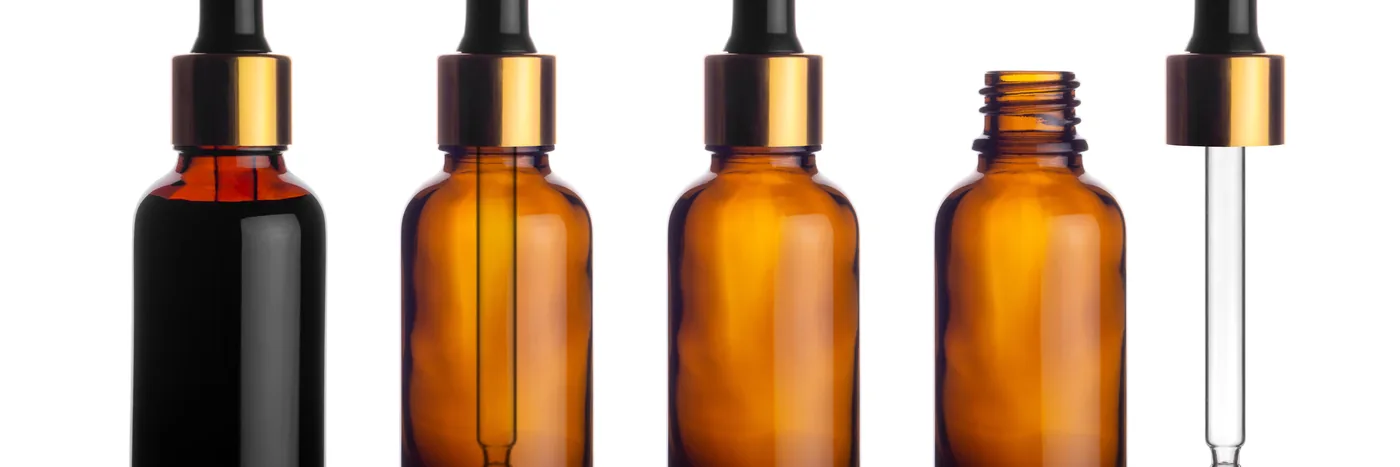 Five unlabelled amber glass serum bottles of different sizes lined up side by side with a glass pipette, on a plain white background.