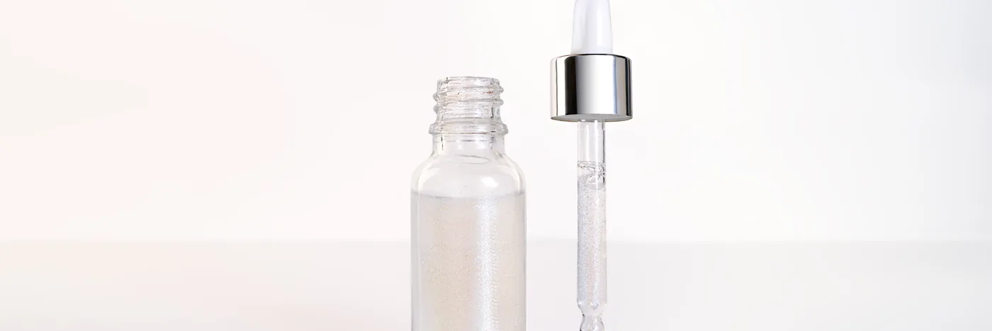 An open unlabelled glass serum bottle beside its separated dropper pipette, both on a plain white surface.
